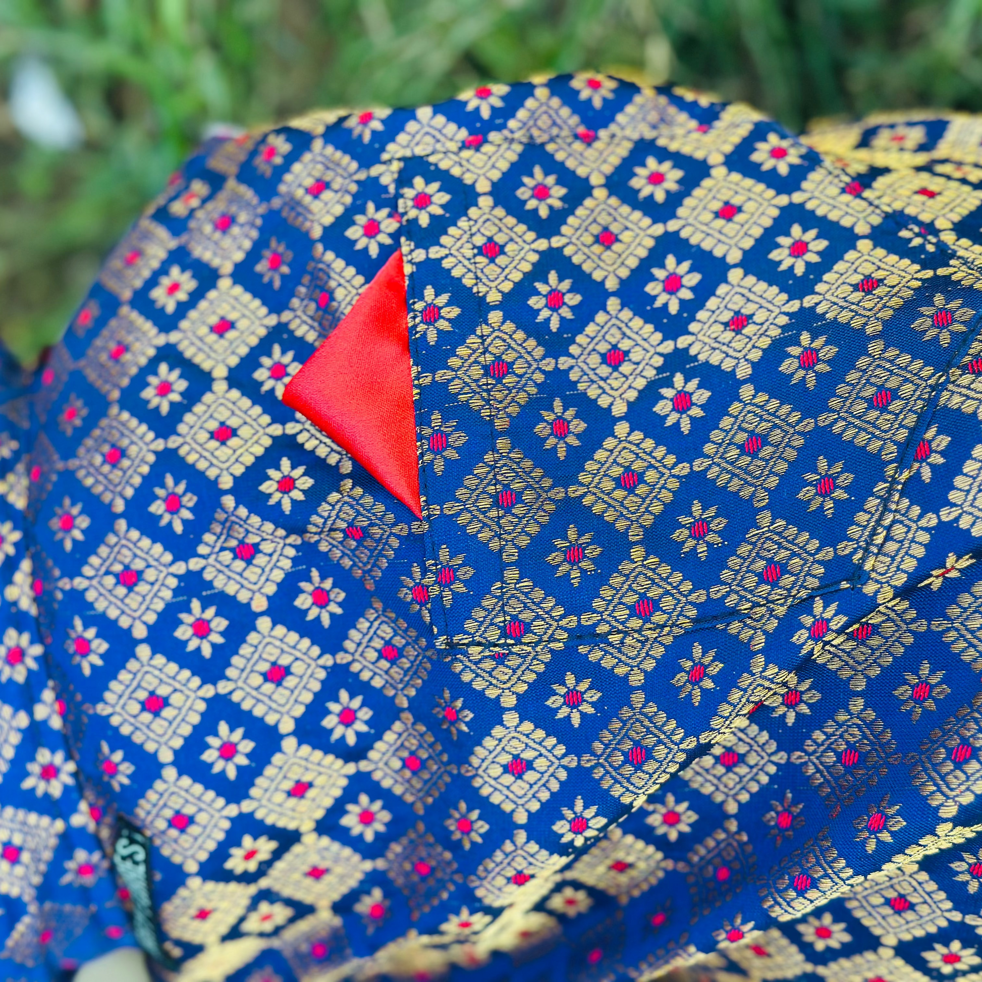 Blue fabric with gold and red pattern, featuring a red triangle on a blurred green background